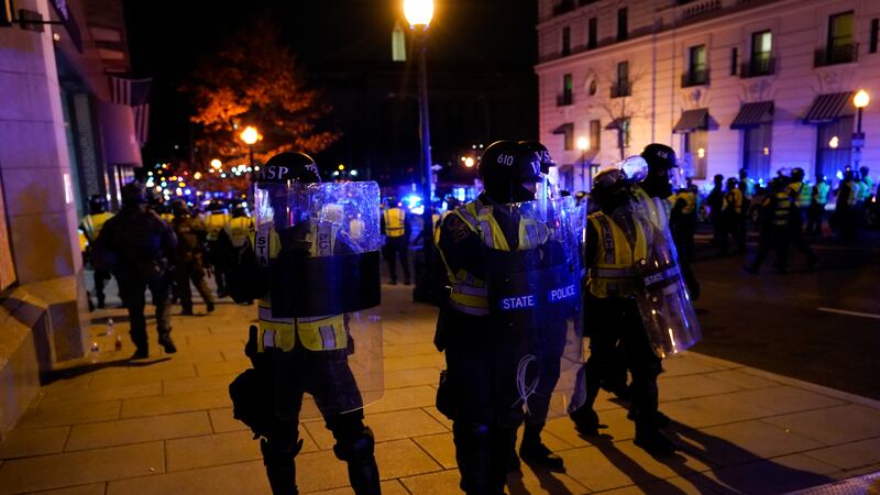 A police line moves to clear people from the front of a hotel who were violating curfew in...